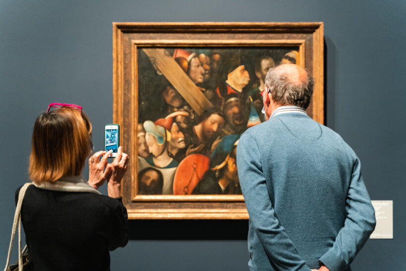Een ouder koppel kijkt naar een werk van Bosch. De dame maakt een foto met haar smartphone.