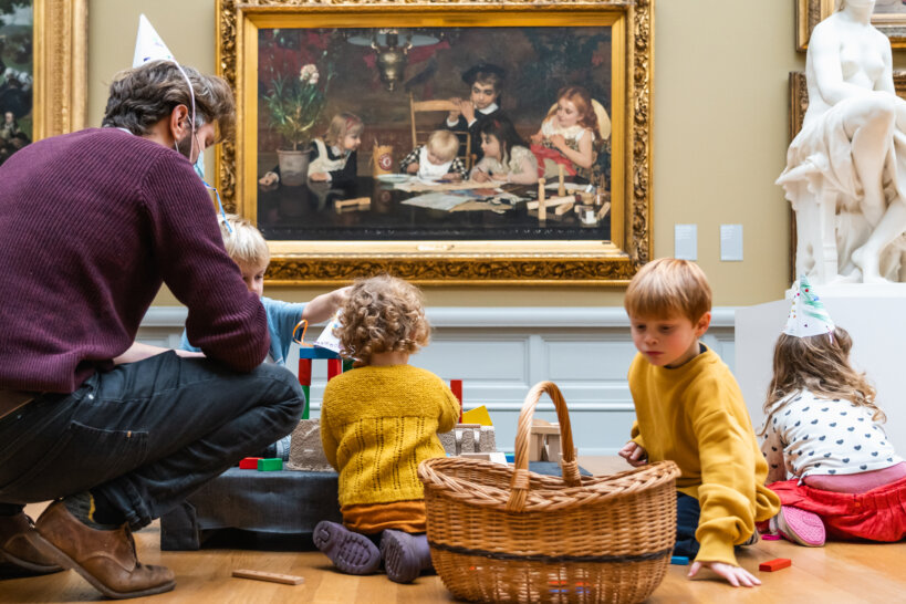 Een vader met drie kinderen zitten voor het schilderij 'De Meesterschilders' in het MSK.